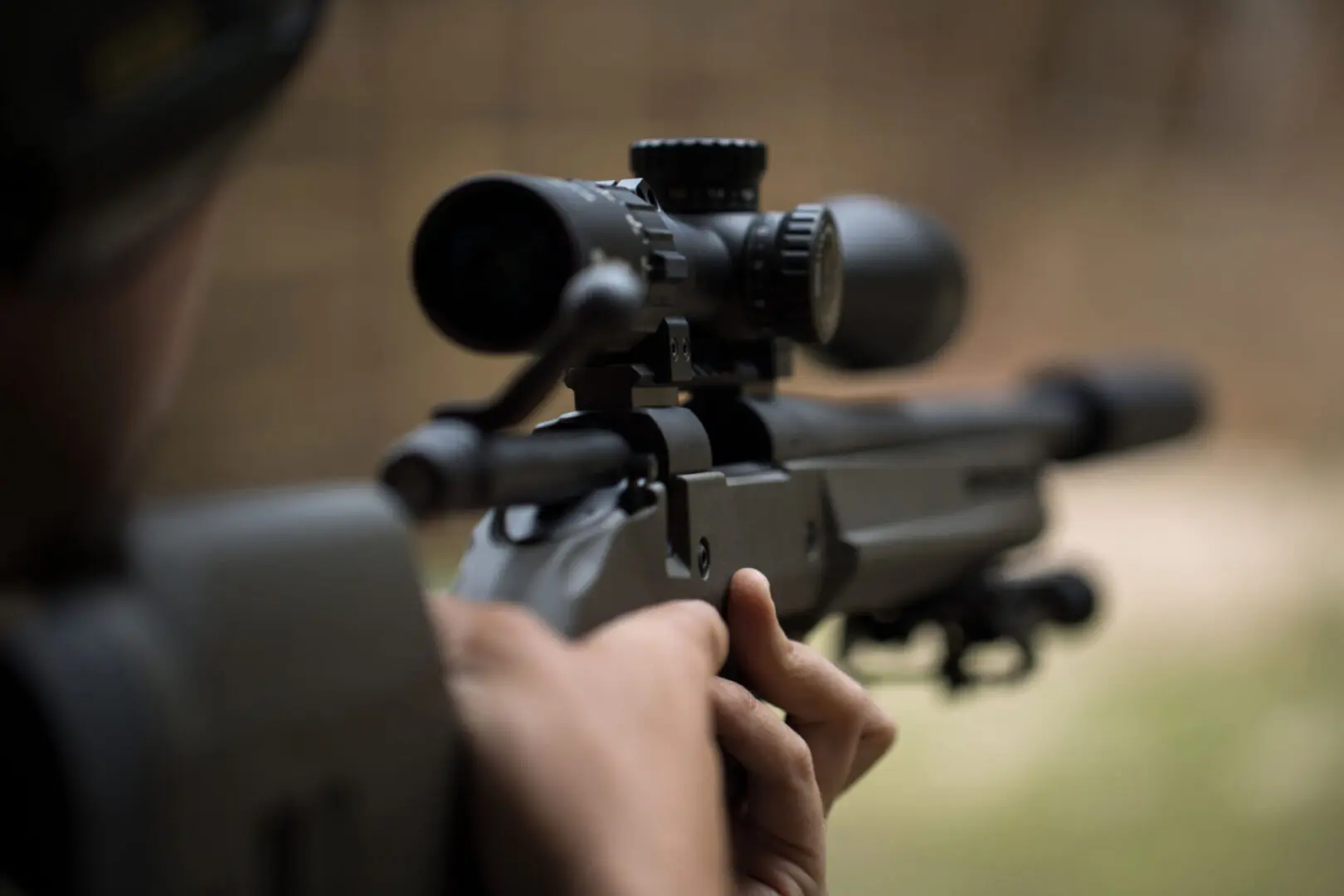 Person aiming rifle with scope, blurred background.