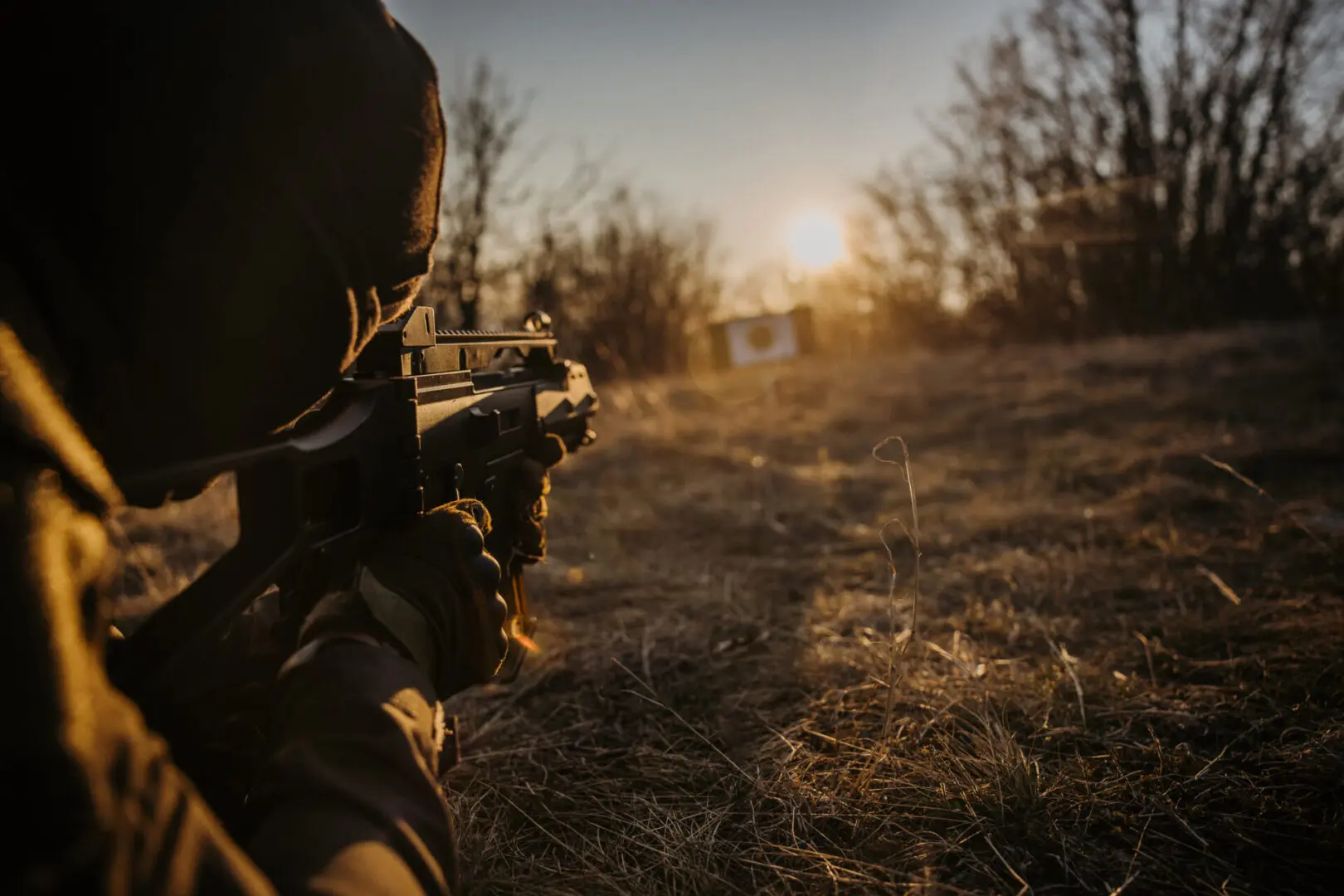 Person aiming rifle at distant target outdoors.