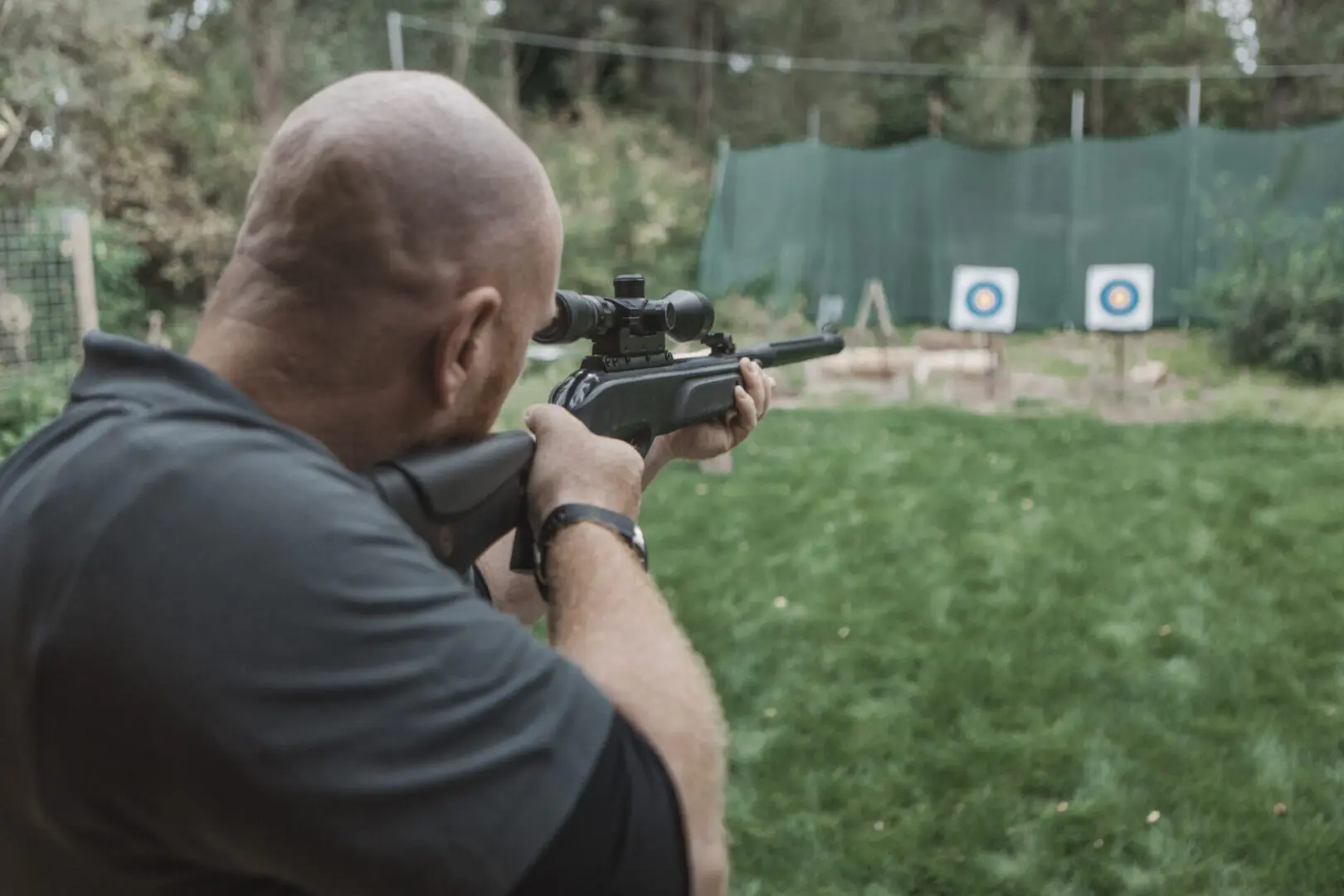 Man aiming rifle at distant targets outdoors.