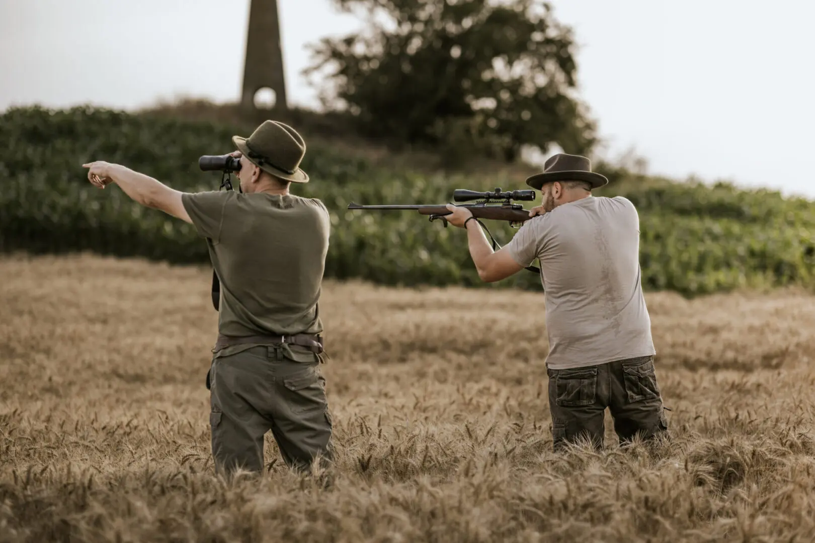 Two hunters aiming rifles in field.
