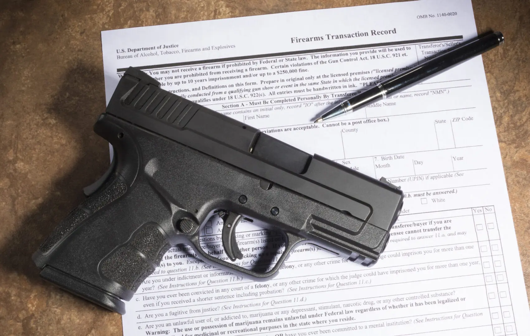 Handgun on firearm transaction record with pen.