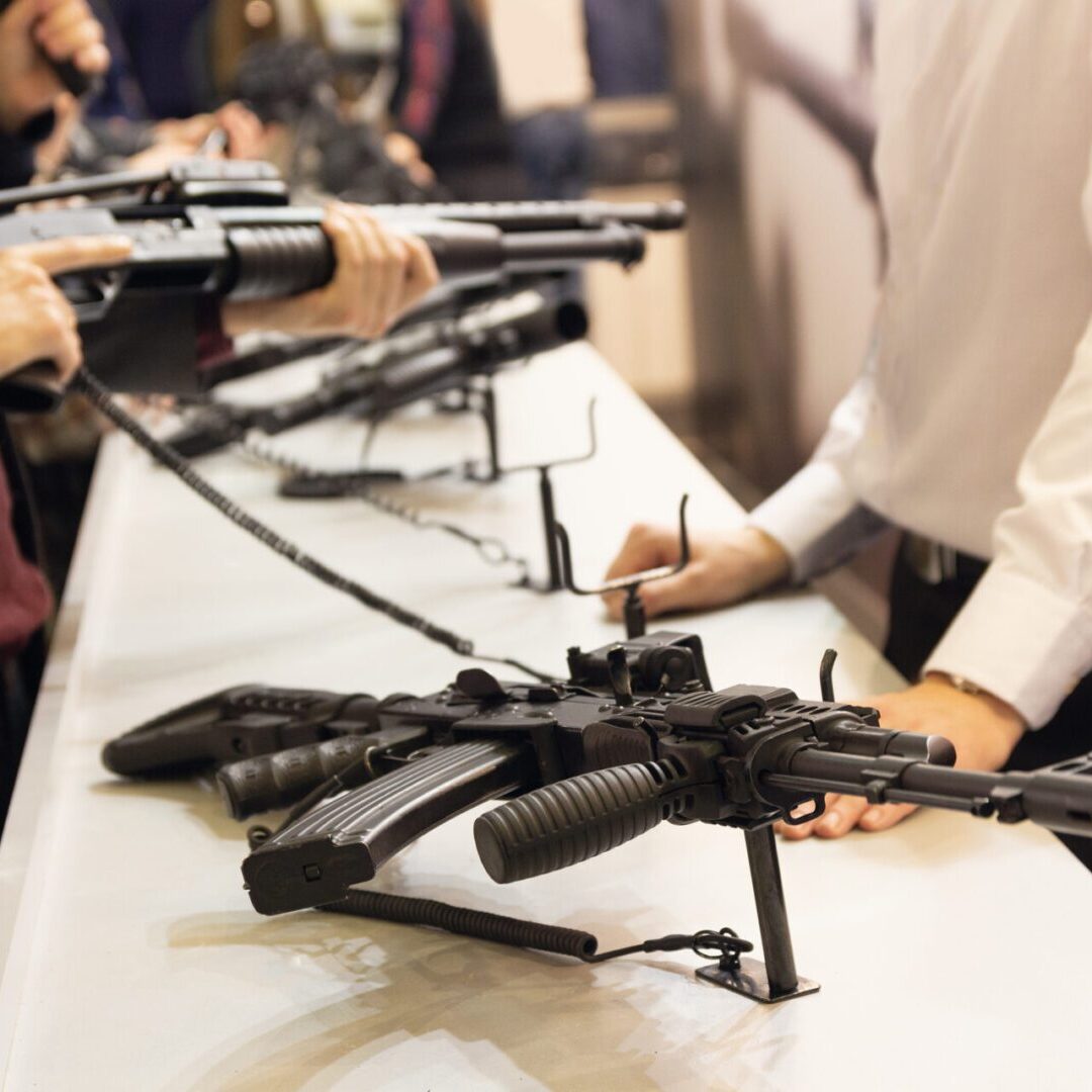 People examining rifles on a display table.